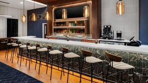 Una zona de bar con mostrador de mármol, varios taburetes, lámparas colgantes y una cafetera.