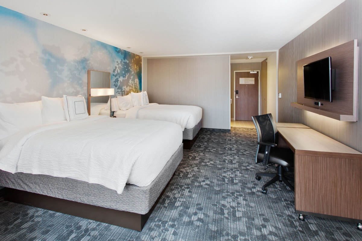 A hotel room with two beds, a desk, a TV, and a carpeted floor.