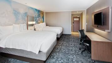 A hotel room with two beds, a desk, a TV, and a carpeted floor.