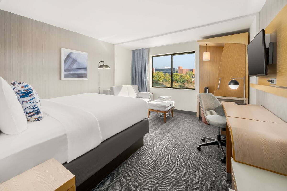 A hotel room with a bed, desk, chair, and a TV.