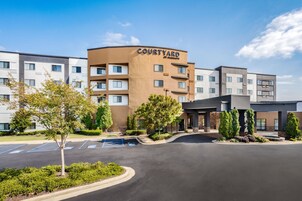 Un hotel Courtyard by Marriott con aparcamiento, zonas ajardinadas y una fachada de edificio moderna.