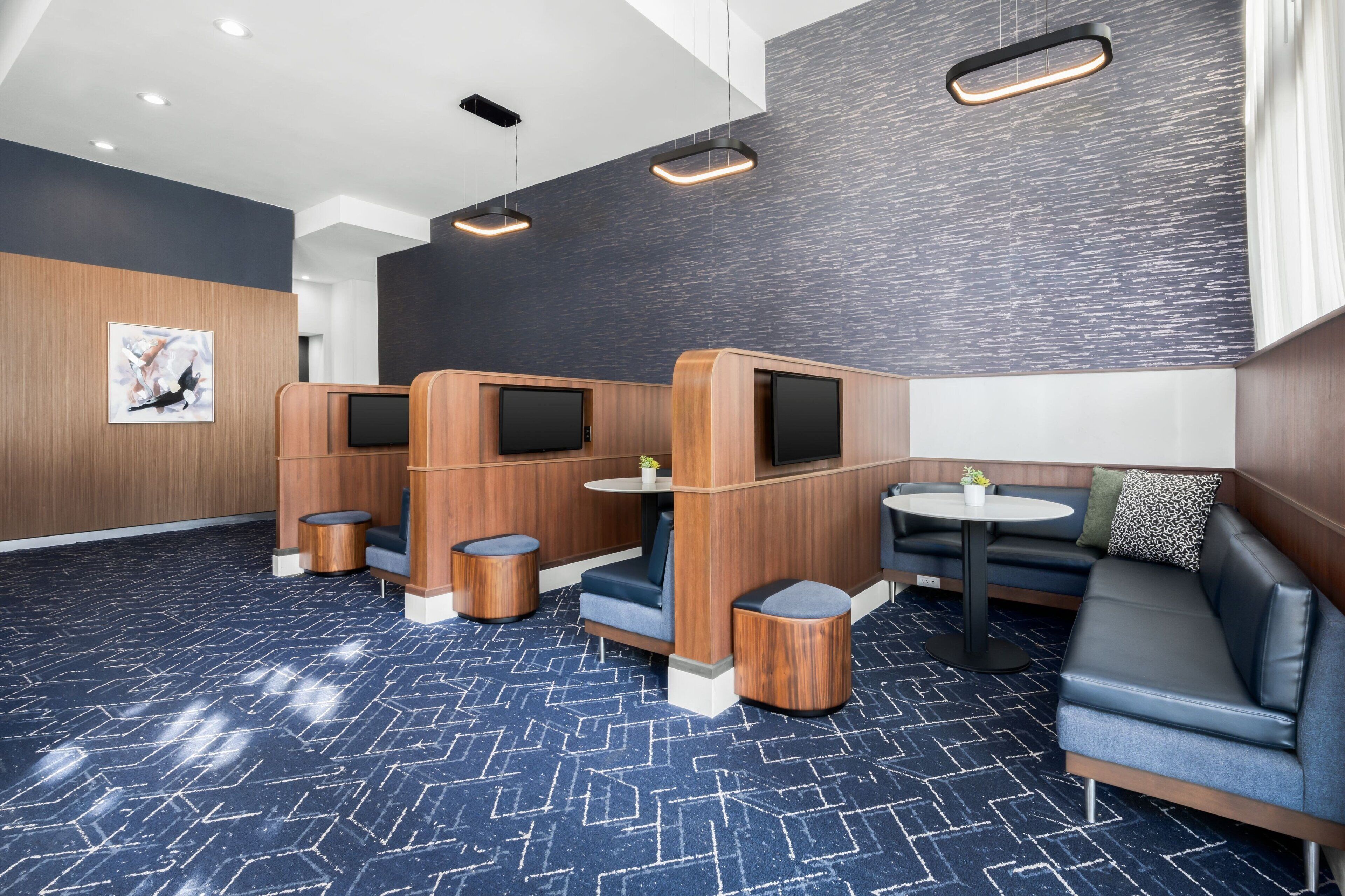 A modern hotel lobby with seating areas, a reception desk, and a large artwork on the wall.