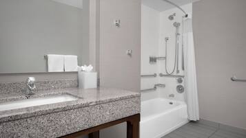 A bathroom with a granite countertop sink, a mirror, a shower with a curved glass door, and a bathtub.