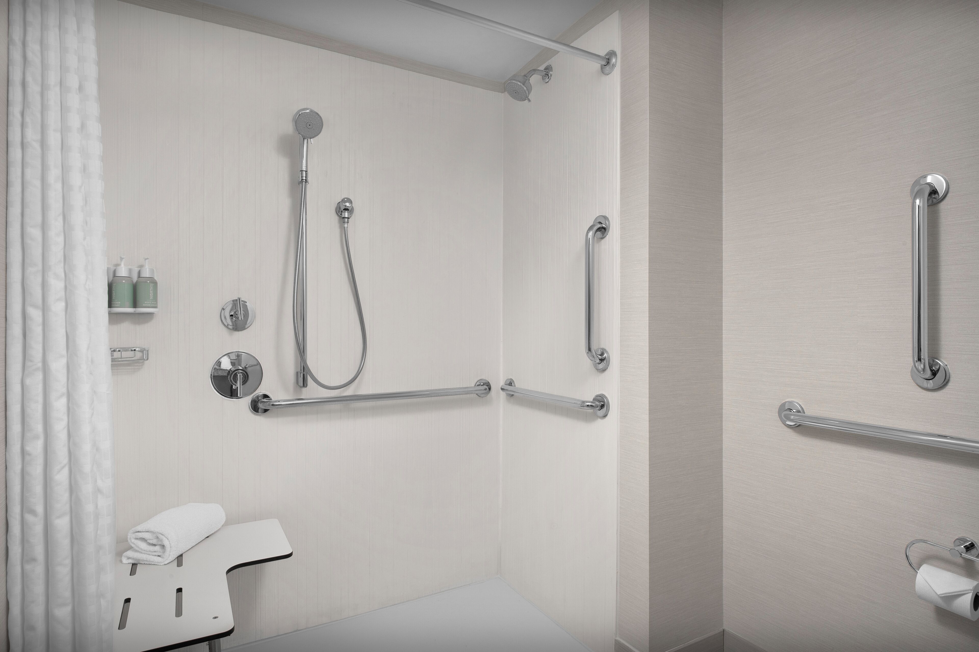 A modern bathroom with a shower, grab bars, a towel rack, and a toilet paper holder.