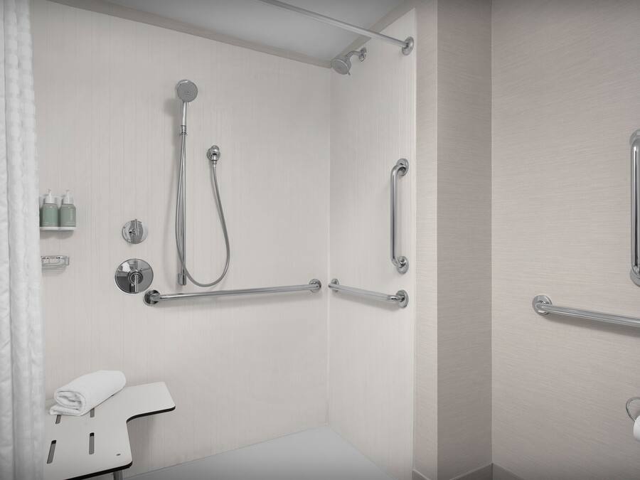 A modern bathroom with a shower, grab bars, a towel rack, and a toilet paper holder.