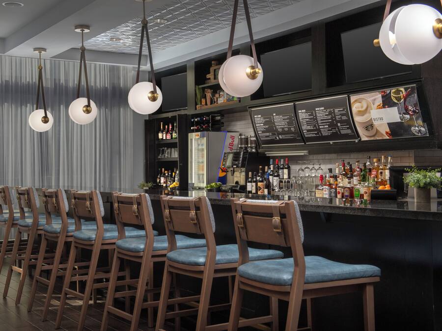 Eine Bar mit mehreren Holzhockern, hängenden Pendelleuchten und einer gut sortierten Bar.