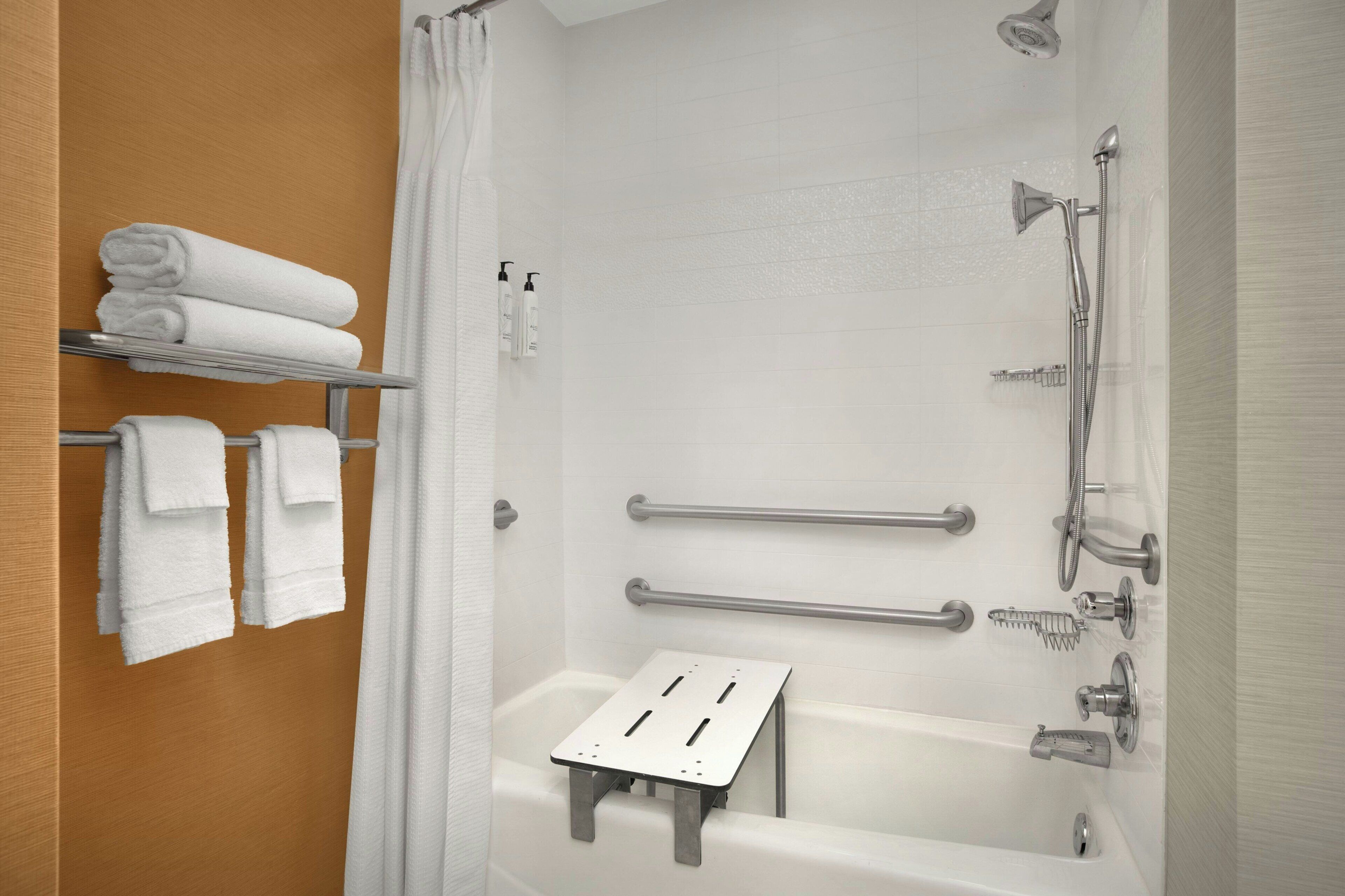 A modern bathroom with a bathtub, shower, and handrails.