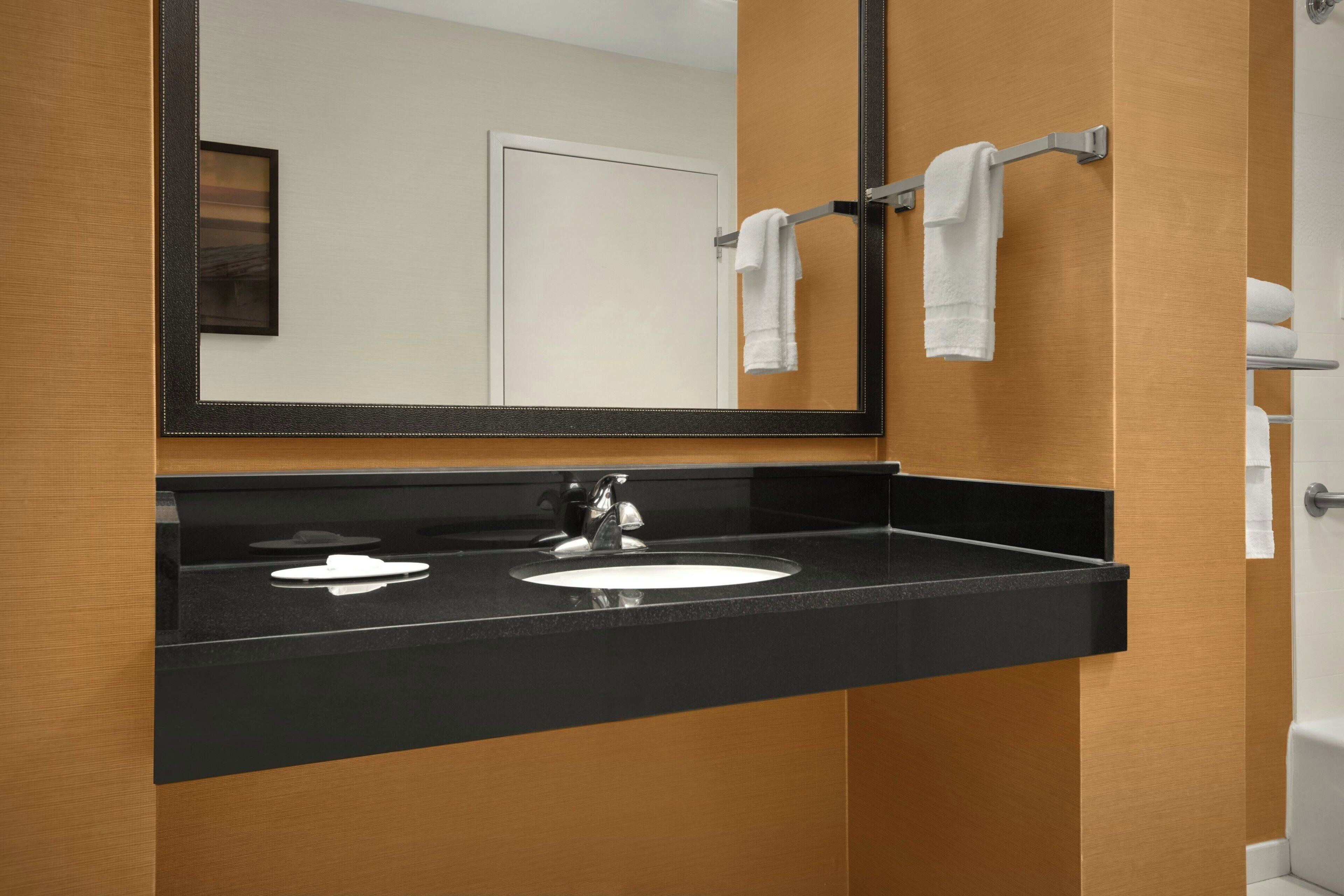 A bathroom with a black countertop sink, a mirror, and a towel rack.
