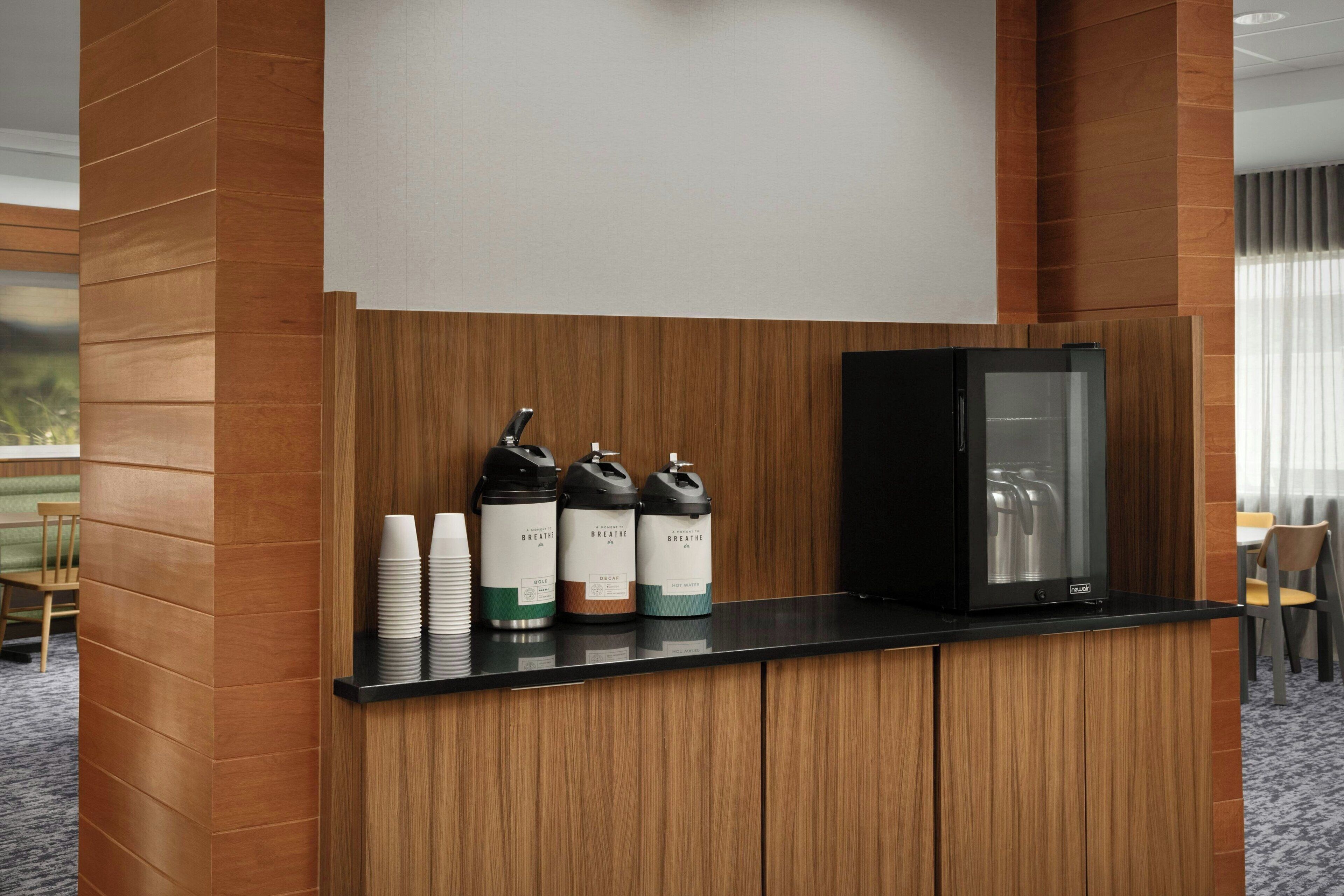 A reception area with a black cabinet, three water dispensers labeled 'BREATHE,' and a stack of white paper cups.
