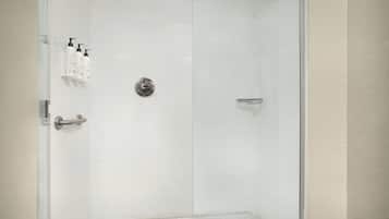 A modern bathroom with a glass shower enclosure, white tiled walls, and a metal shower control panel.