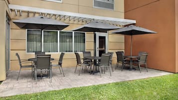 An outdoor patio area with a seating arrangement of tables and chairs, covered by umbrellas.