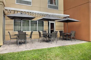 Un patio al aire libre con una disposición de mesas y sillas, cubierto por sombrillas.