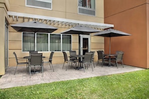 An outdoor patio area with a seating arrangement of tables and chairs, covered by umbrellas.