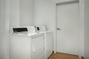 Une buanderie blanche avec un lave-linge et un sèche-linge à chargement frontal, une porte et un plancher en bois.