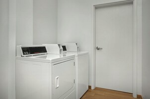 A white laundry room with a front-loading washer and dryer, a door, and a wooden floor.