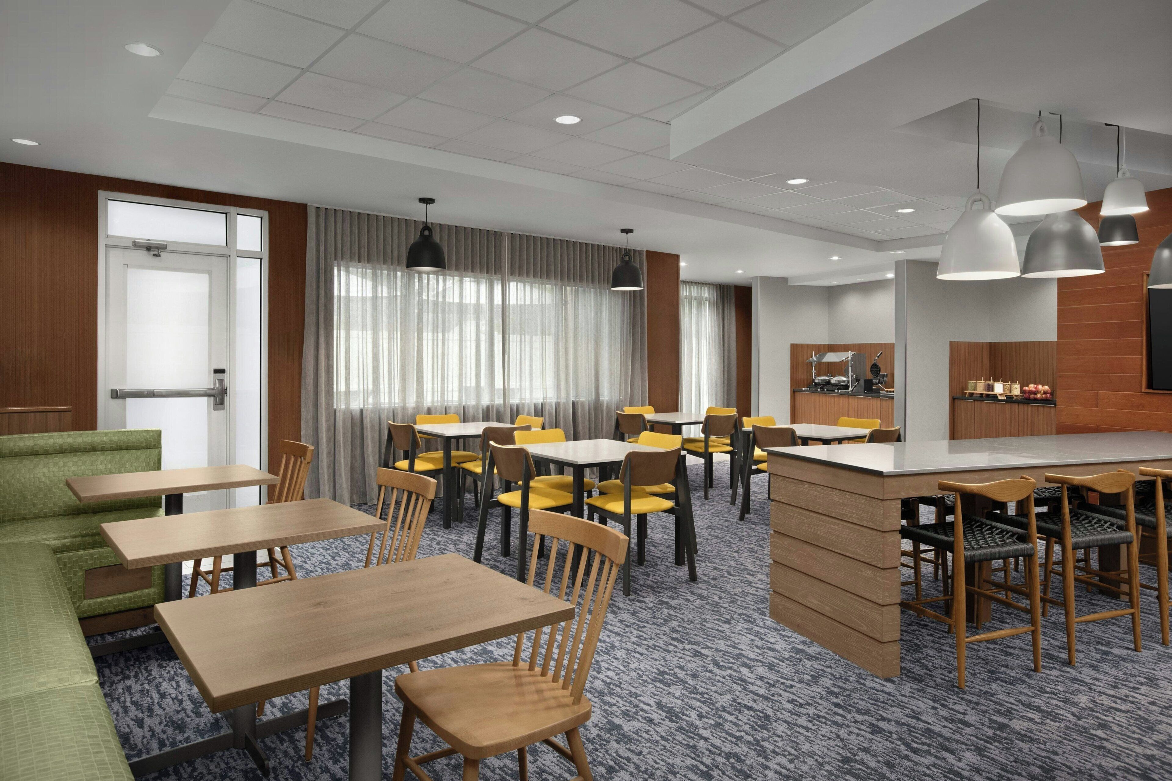 Een restaurantgedeelte in een hotel met meerdere tafels en stoelen, een bar en uitzicht op de stad.