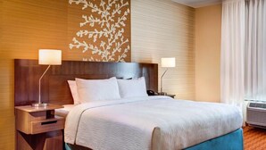 A hotel room with a large bed, two bedside tables with lamps, a decorative wall panel, and an air conditioning unit. - Fairfield Inn & Suites Wilmington New Castle (New Castle)