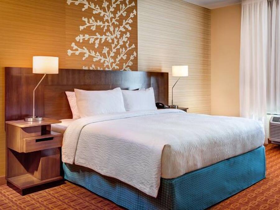 Habitación de hotel con una cama grande, dos mesitas de noche con lámparas, un panel decorativo en la pared y un equipo de aire acondicionado.