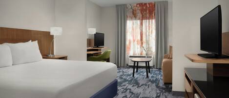 A hotel room with a large bed, a desk with a computer, a television, and a chair.