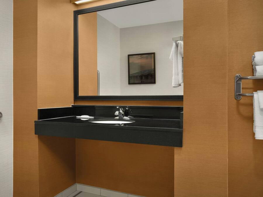 Un baño con lavamanos de superficie negra, un espejo y un perchero para toallas.