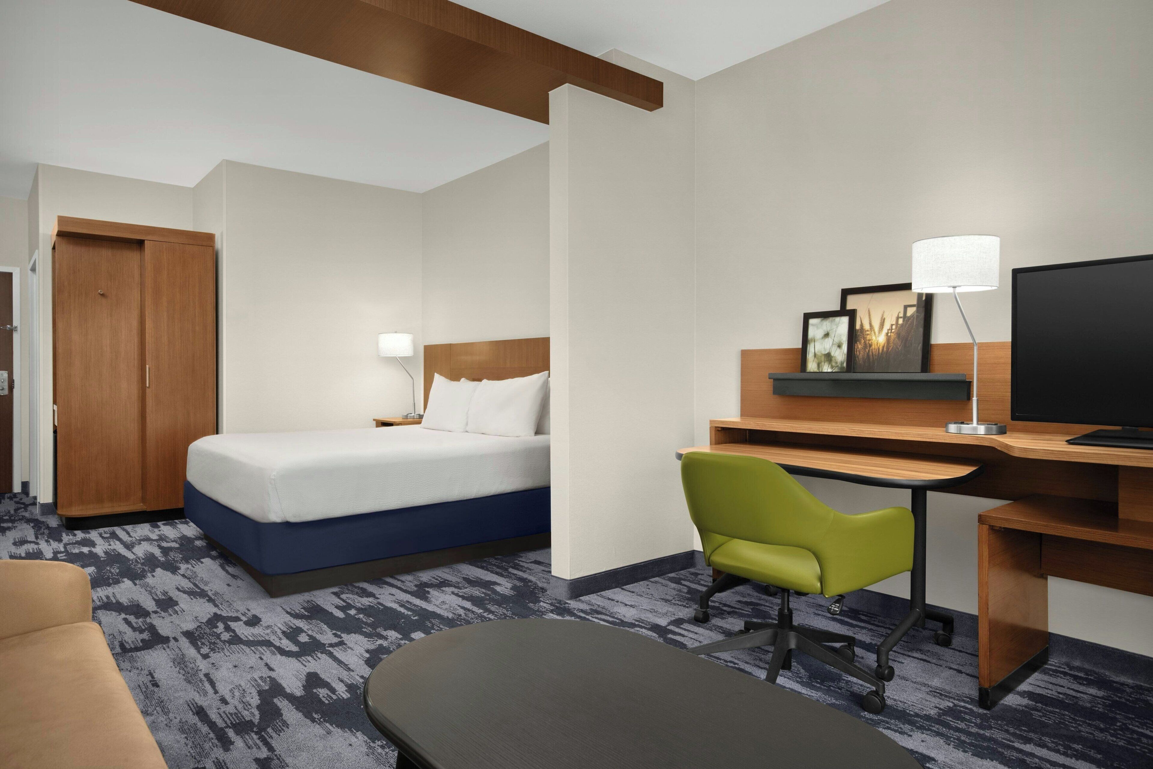 A hotel room with a bed, a desk with a chair, a television, and a door.