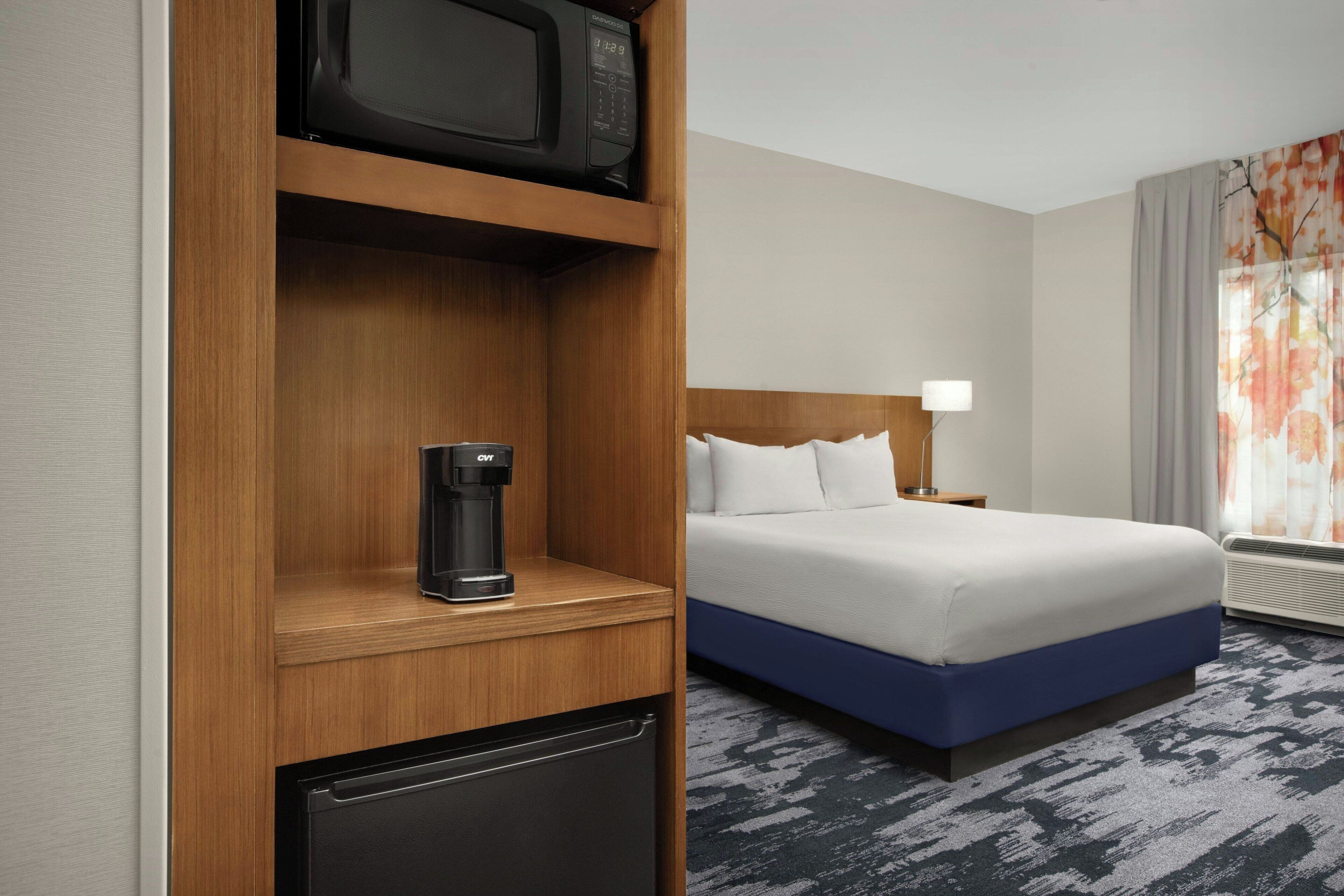 A hotel room with a bed, a coffee maker, a microwave, and a mini-fridge.
