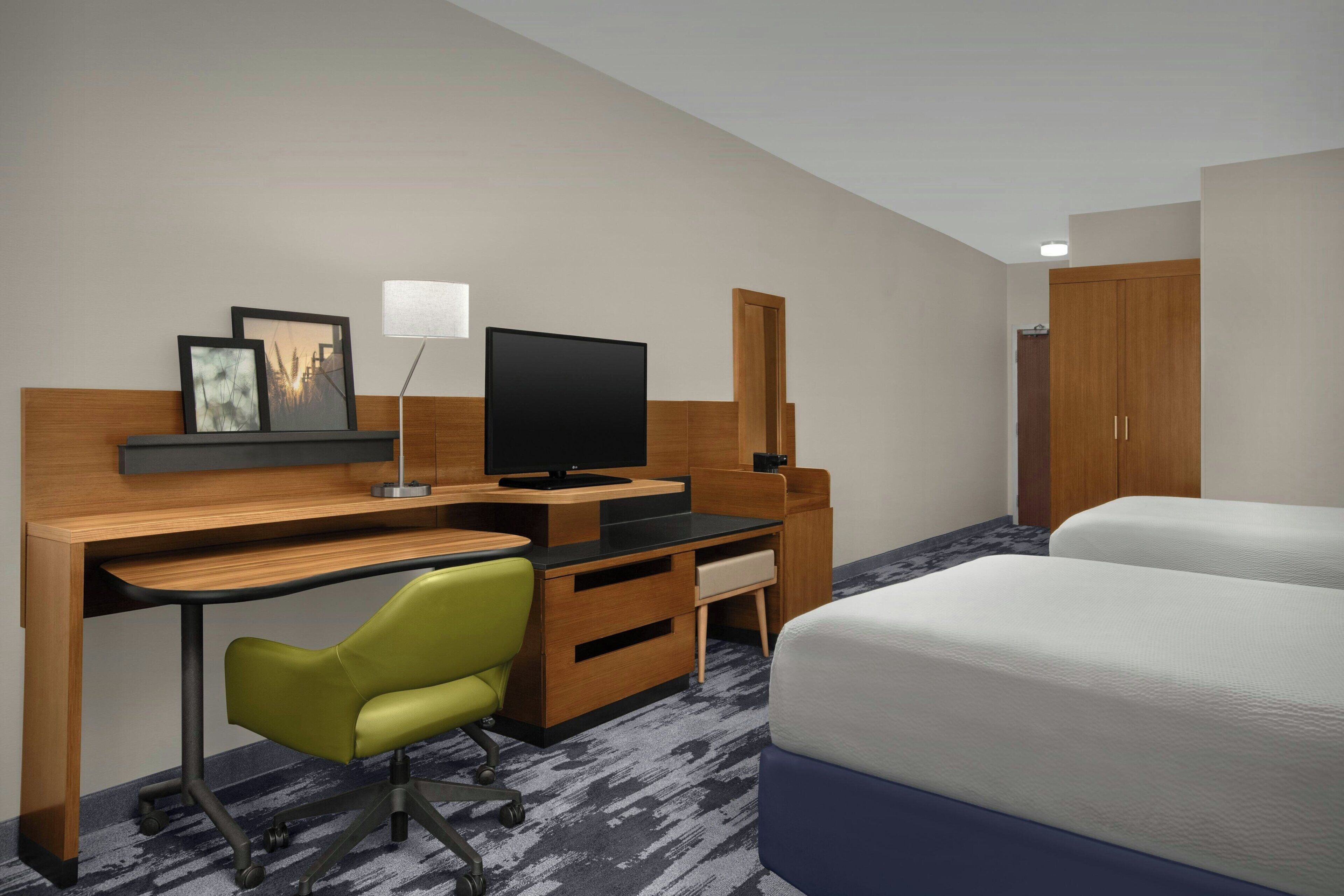 A hotel room with a desk, a television, a chair, a bed, and a wardrobe.