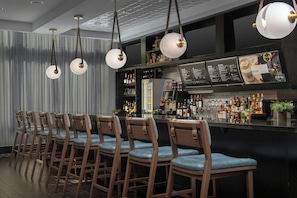 A bar area with wooden bar stools, hanging pendant lights, and a menu board.