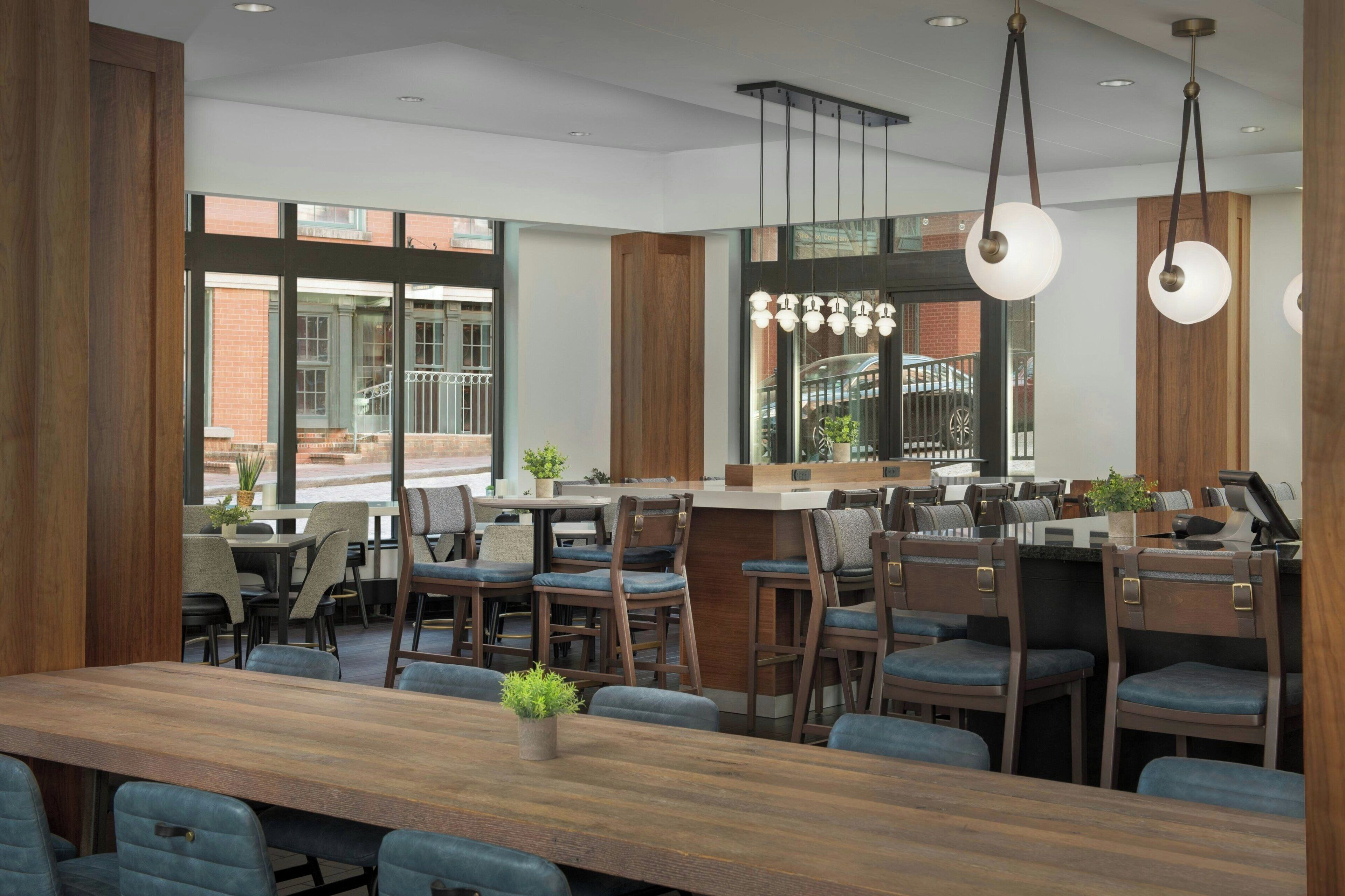 Un restaurant moderne avec une longue table en bois, des chaises rembourrées en tissu bleu et des luminaires suspendus.