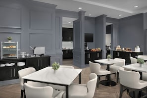 Une cuisine moderne avec des meubles de couleur sombre, un îlot central et un coin repas avec des chaises et des tables blanches.