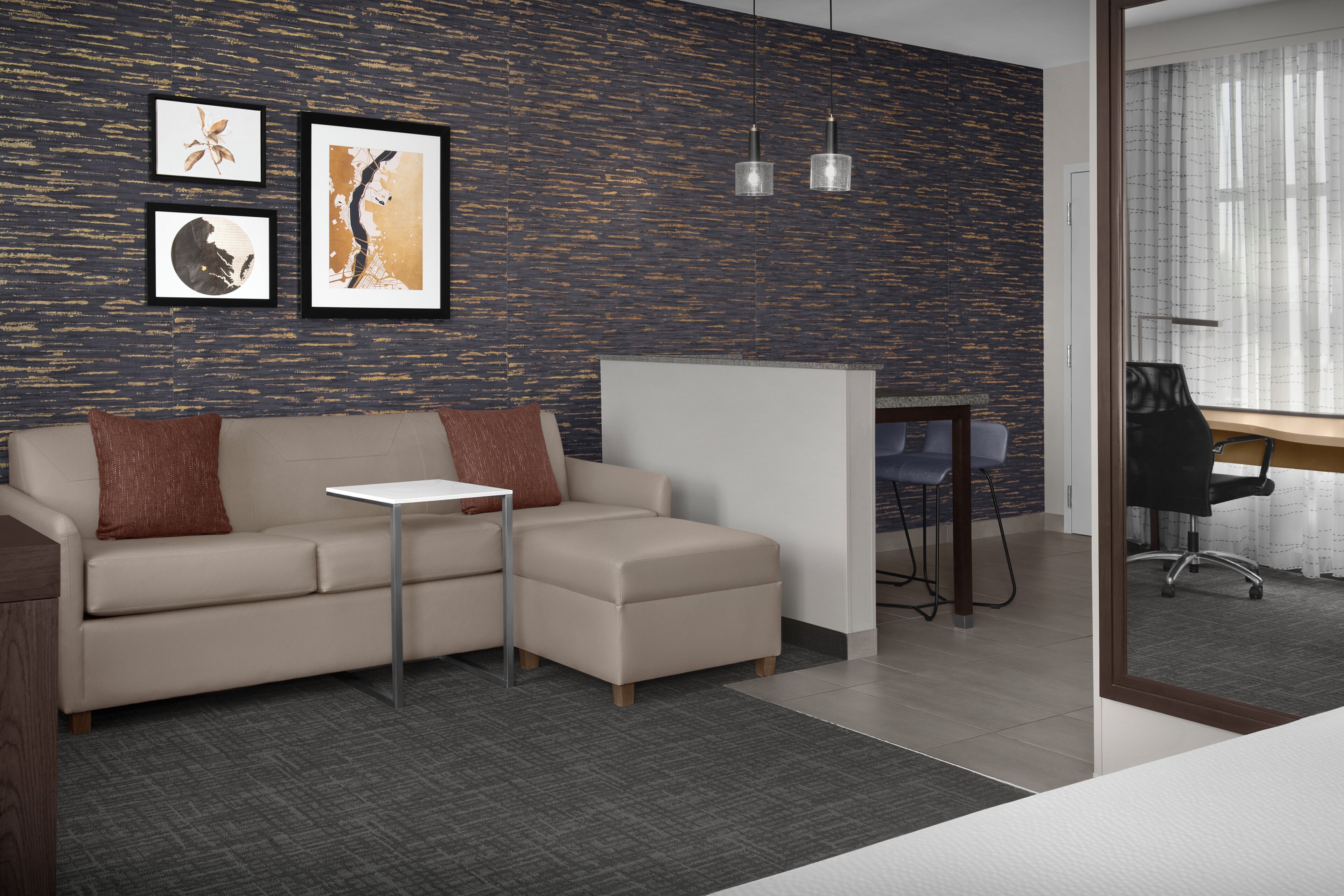Ein moderner Arbeitsraum mit Sofa, einem kleinen Tisch, gerahmten Kunstwerken an der Wand und einem Schreibtisch mit Stuhl.