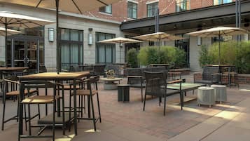 Un patio al aire libre con mesas, sillas, sombrillas y un edificio de ladrillo al fondo.