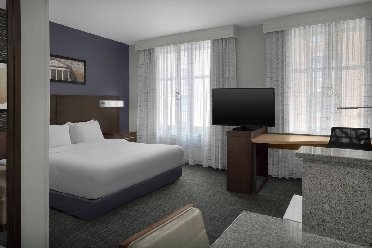 A hotel room with a bed, a desk, a television, and curtains.