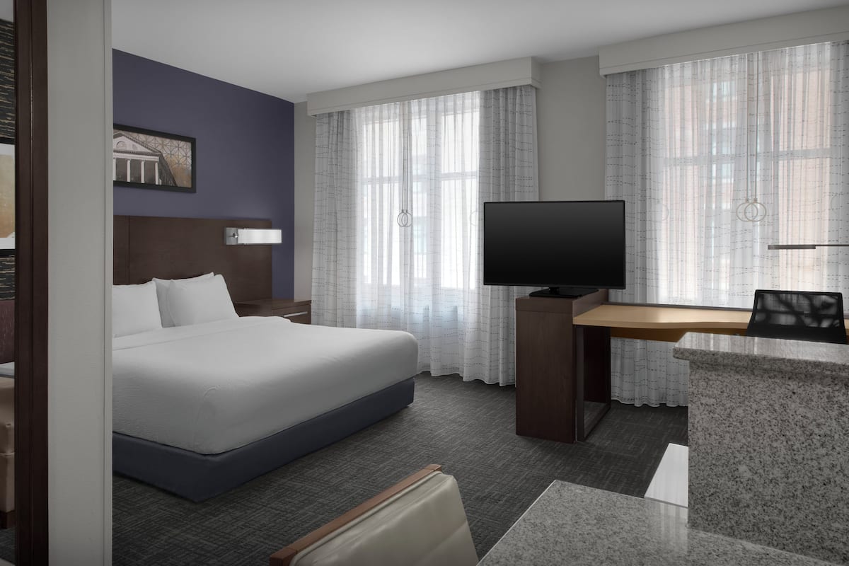 A hotel room with a bed, a desk, a television, and curtains.