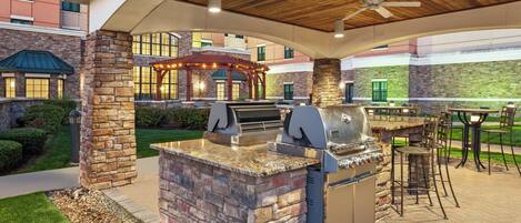 An outdoor patio with a stone barbecue station, seating area, and a covered gazebo.