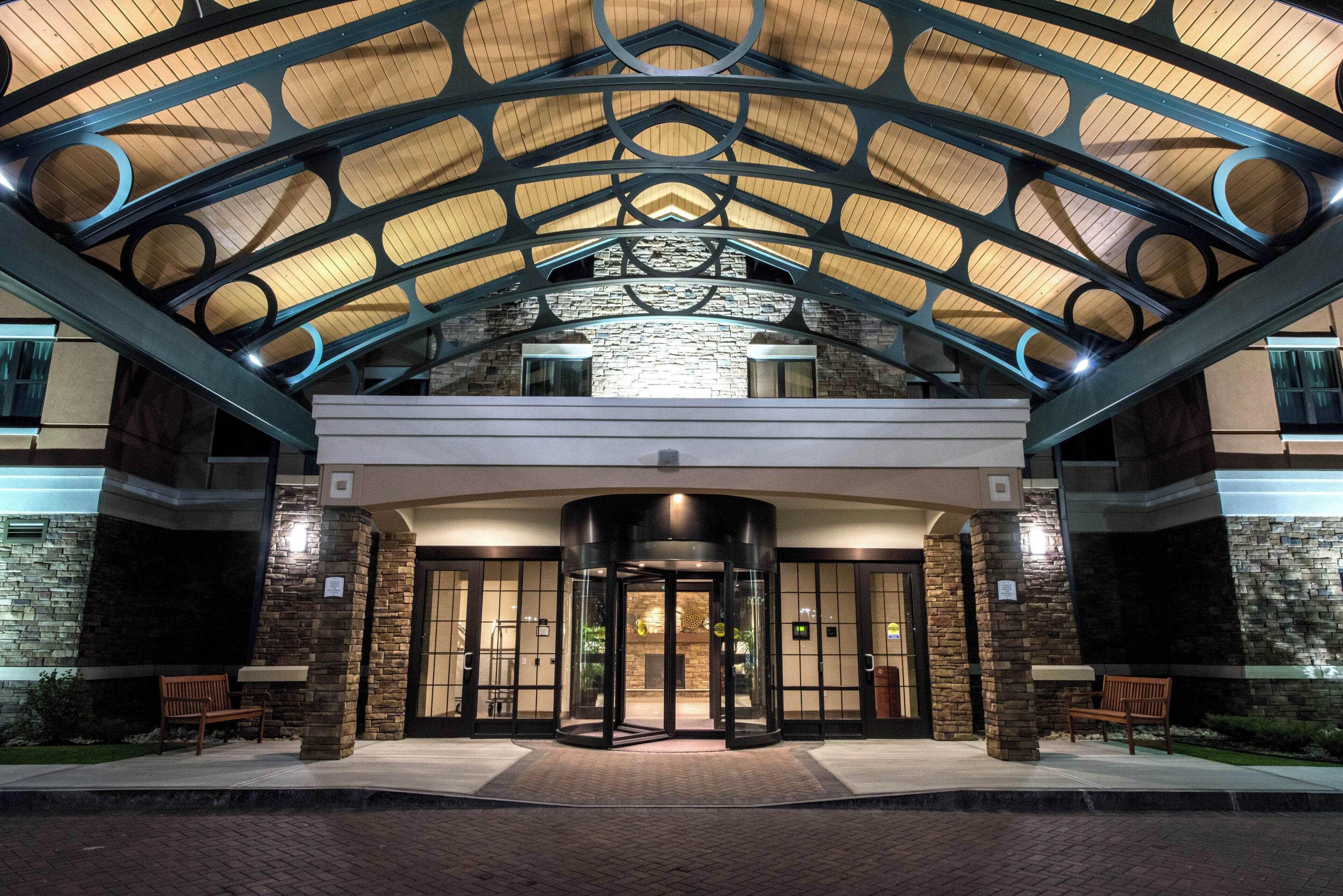 L’entrée d’un hôtel au design moderne, caractérisée par une porte d’entrée en verre, une façade en pierre et une structure de toit en métal.