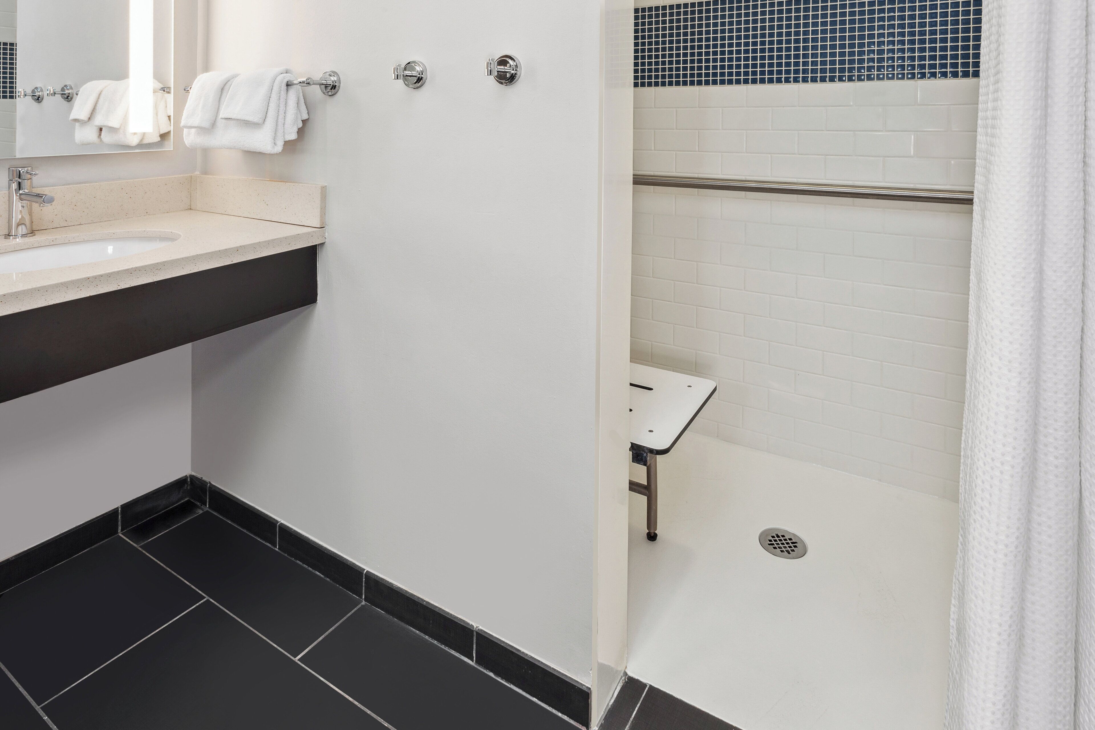 A modern bathroom with a sink, mirror, towel rack, and a shower area with a tiled wall and a drain.