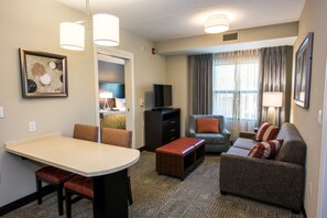 Une chambre d’hôtel comprenant un coin repas, un ensemble de canapés, une télévision et une grande fenêtre avec des rideaux.