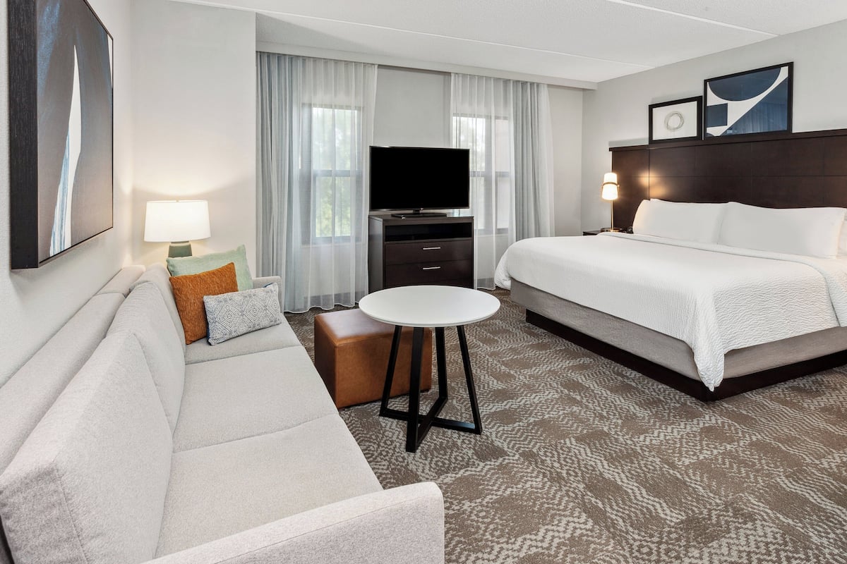 Une chambre d’hôtel avec un lit, un canapé, une télévision, une lampe et une petite table.