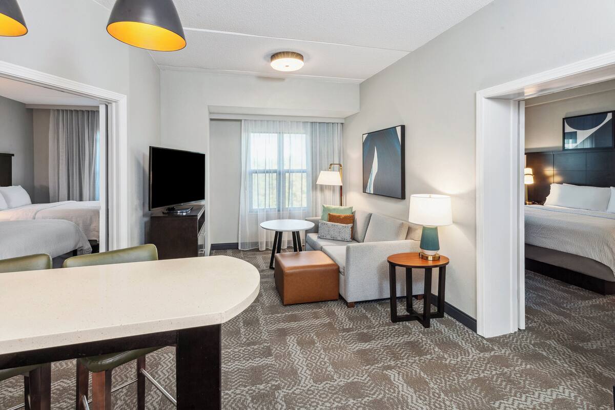 Une chambre d’hôtel avec un lit, un canapé, une table à manger, une télévision et une fenêtre avec des rideaux.