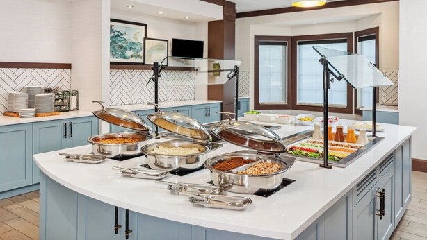A buffet setup with various food items and serving utensils. - Staybridge Suites Albany Wolf Rd-Colonie Center by IHG (Albany)