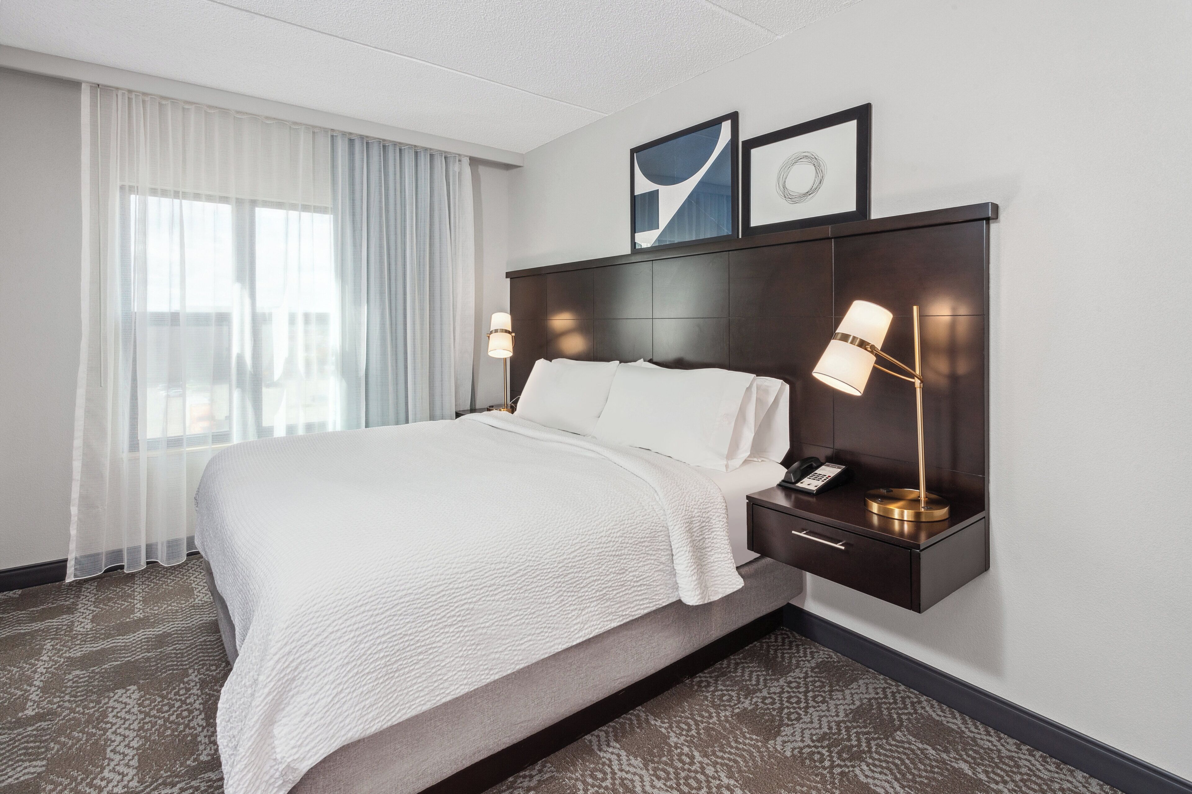 Hotelkamer met een groot bed, nachtkastje met een lamp en uitzicht op de stad.