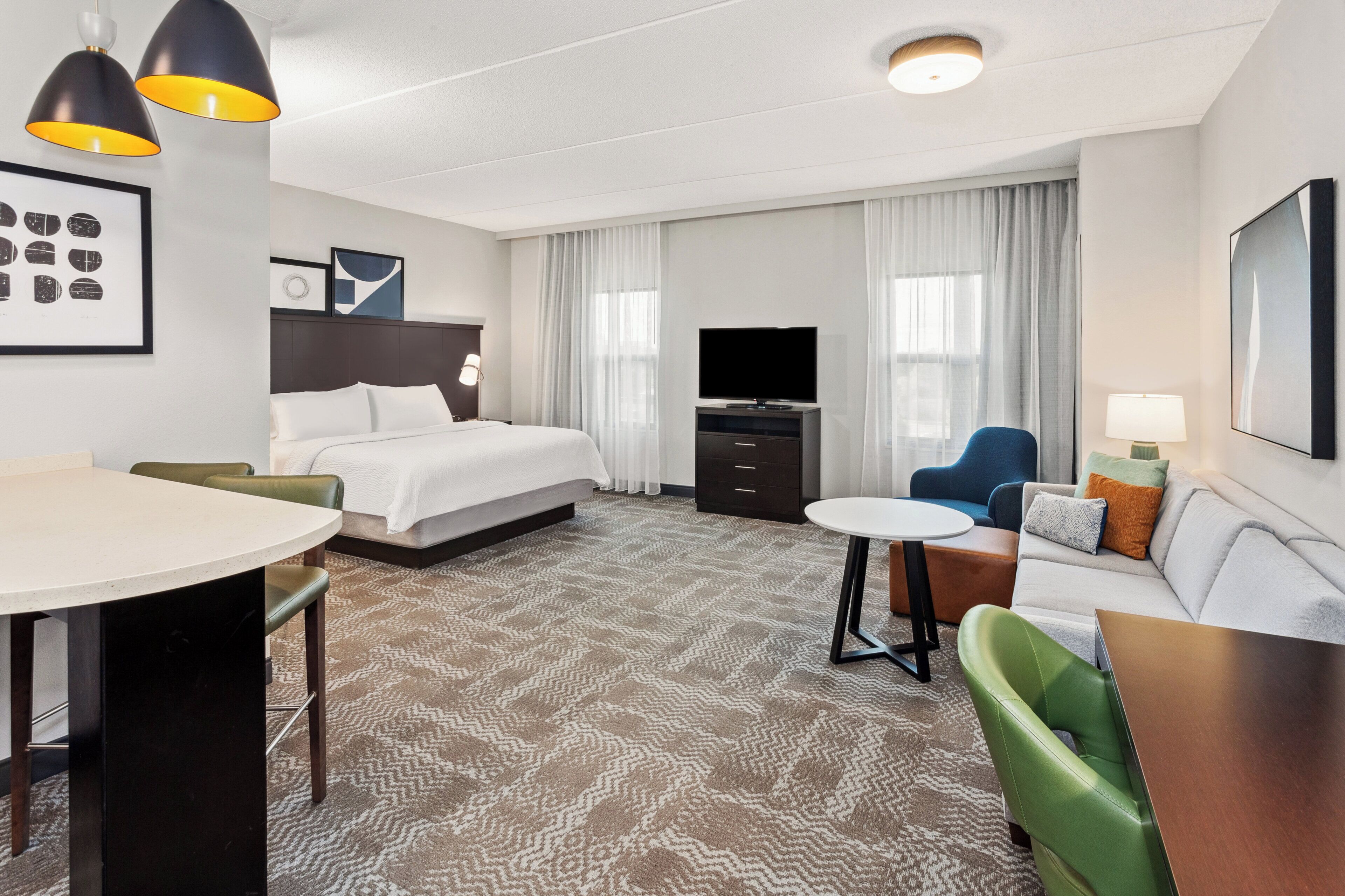 A hotel room with a bed, a desk, a sofa, a TV, and a dining area.