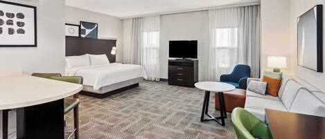 A hotel room with a bed, a desk, a sofa, a TV, and a dining area.