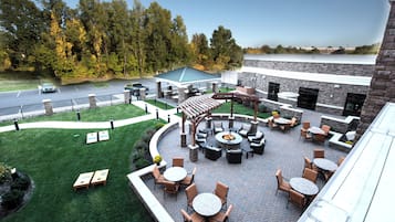 An outdoor patio area with seating and a fire pit, surrounded by a brick wall and a view of a parking lot and trees.
