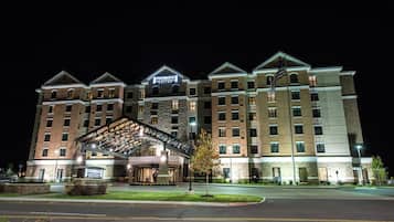 Un hotel de varios pisos con un llamativo letrero de Staybridge Suites, una entrada techada y una fachada bien iluminada.