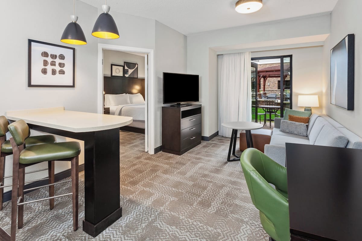Une chambre d’hôtel moderne dotée d’un coin repas, d’un canapé, d’une télévision et d’un balcon avec des sièges d’extérieur.