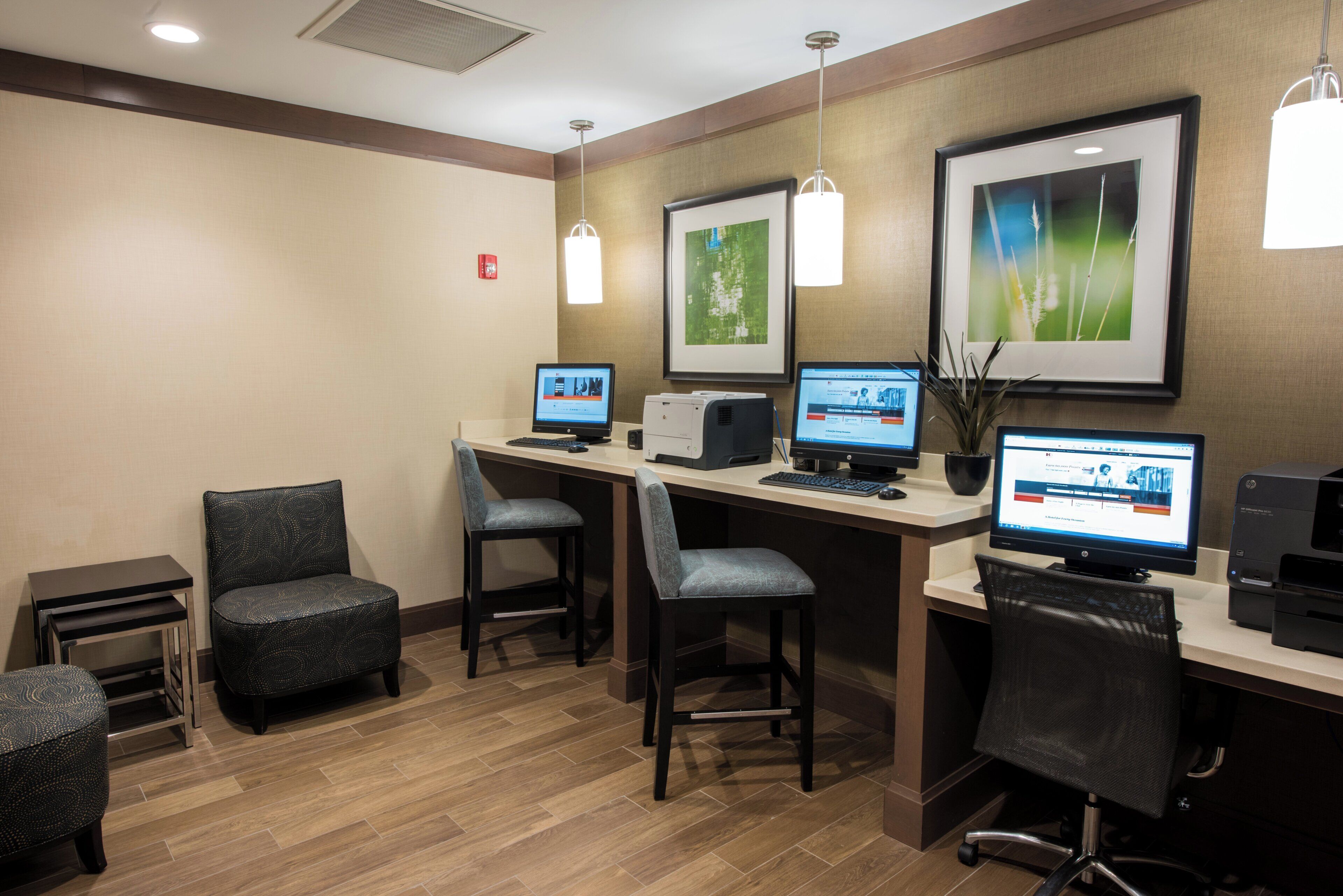 A hotel room with a desk, two chairs, a printer, and two computers.