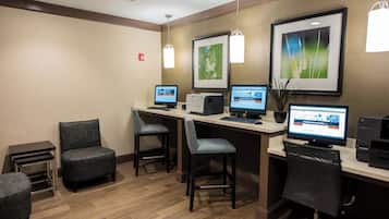 A hotel room with a desk, two chairs, a printer, and two computers.