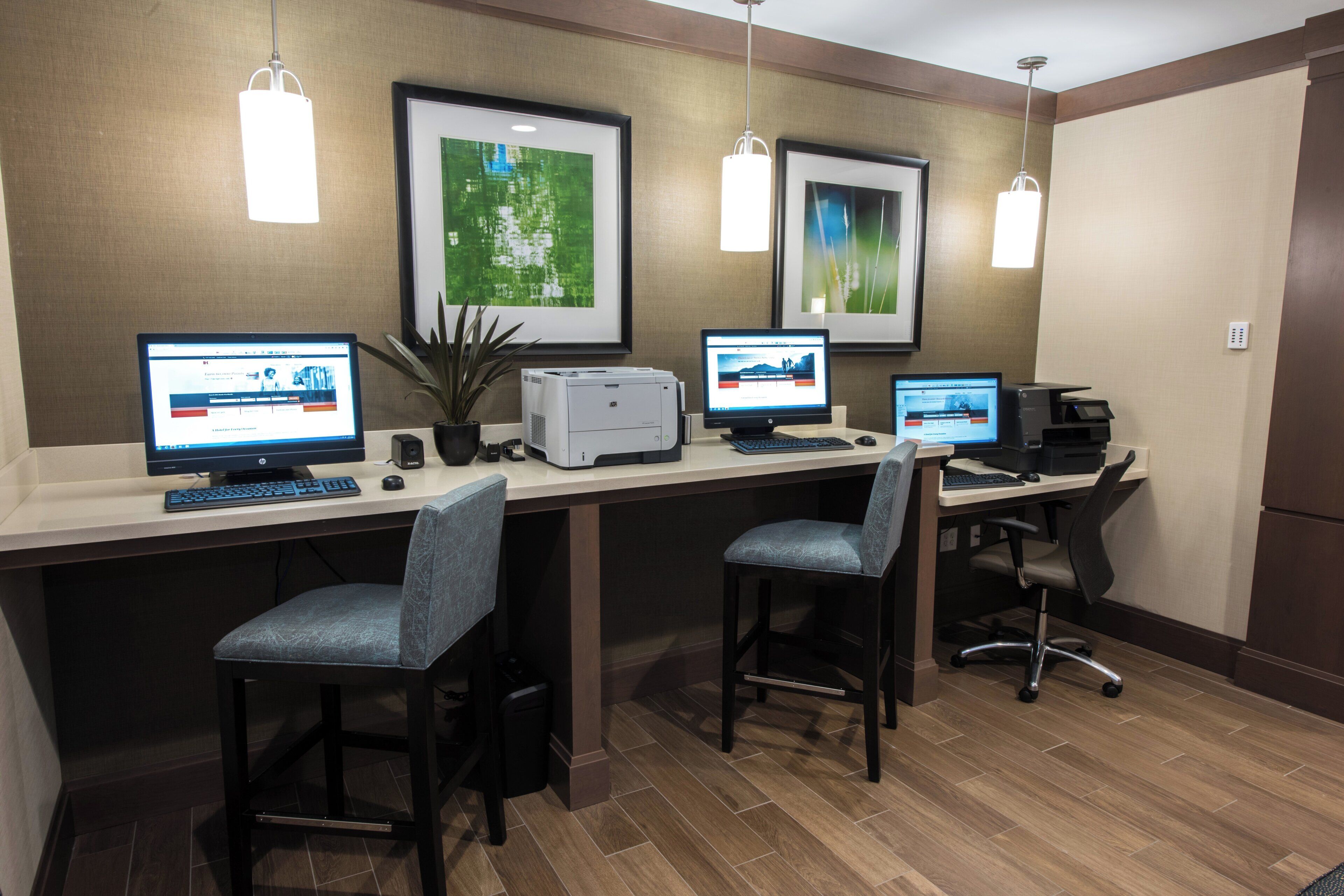 Habitación de hotel con un escritorio, dos computadoras, dos sillas e impresora.